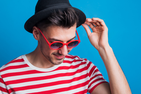 Portrait of a young man in a studio with sunglasses on a blue background.の写真素材