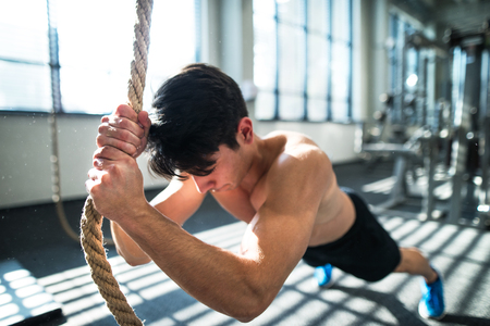 Fit young man in gym working out with climbing rope.の写真素材