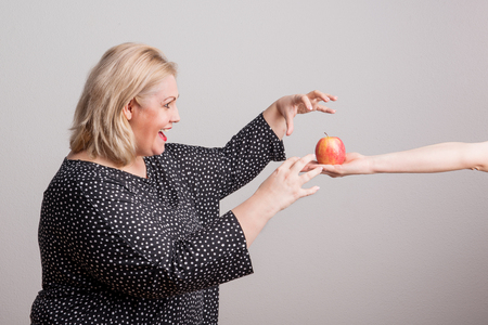 A female hand giving an apple to an attractive overweight woman in studio.の写真素材