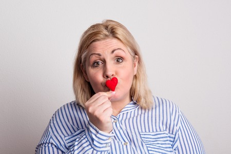 Portrait of an attractive overweight woman holding a heart in front of her lips.の写真素材