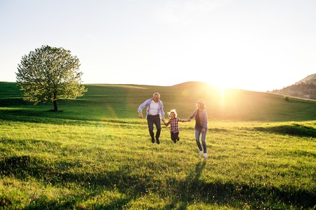 Senior couple with granddaughter on a walk outside in spring nature, jumping.の写真素材