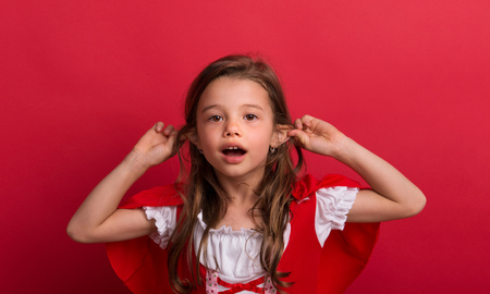 A small girl in Little Red Riding Hood costume in studio on a red background.の写真素材