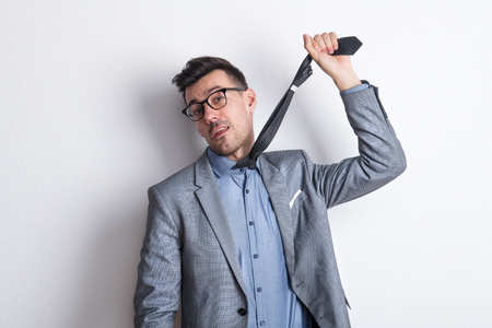 A worried young businessman holding up a tie in a studio.の写真素材