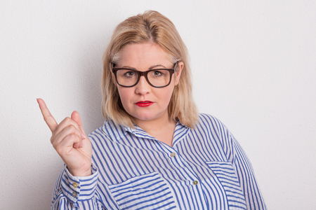 Portrait of a serious overweight woman with glasses in studio, her index finger up.の写真素材