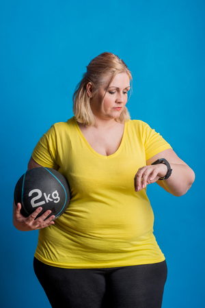 Portrait of a happy overweight woman with smartwatch and heavy ball in studio.の写真素材