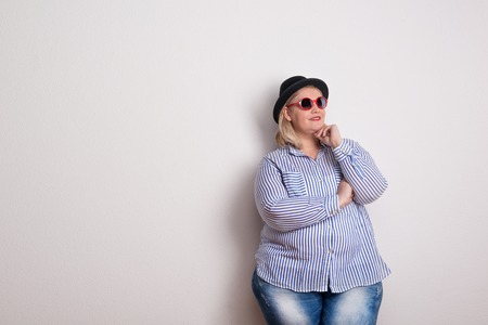 Portrait of an attractive voluptuous woman with hat and sunglasses in a studio.