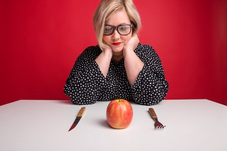 Portrait of an attractive overweight woman in studio, looking at an apple on the table.