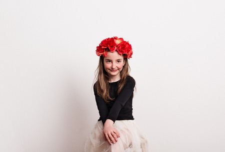A small girl with flower headband sitting in a studio, hands on her knees.の写真素材