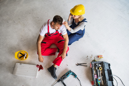 A woman with smartphone helping man worker after an accident at the construction site.の写真素材