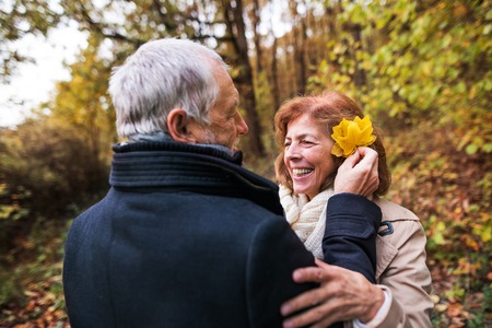 Senior man putting yellow leaves in womans hair in forest in nature.
