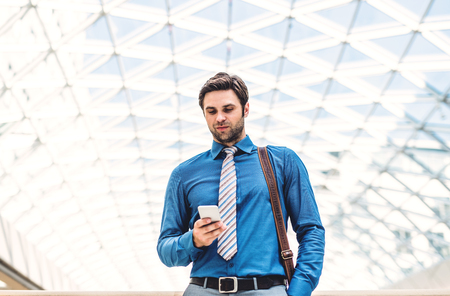 A young businessman with smartphone walking in a modern building, texting.の写真素材