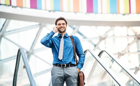 A young businessman going down escalator, talking on the phone. Copy space.の写真素材