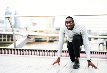 Young sporty black man runner in starting position on the bridge in a city.