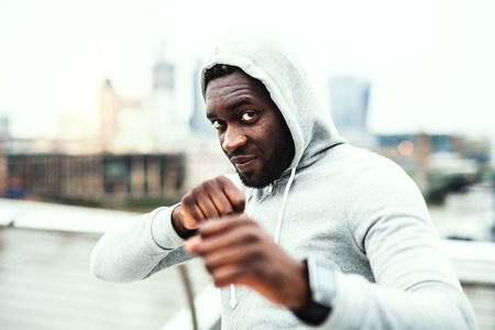 Young active black sportsman in boxing position in a city, wearing hoodie.