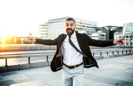 Cheerful hipster businessman walking on the bridge in the city, arms stretched.の写真素材