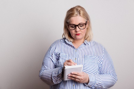 A serious blond overweight woman with glasses and a notepad, making notes.の写真素材