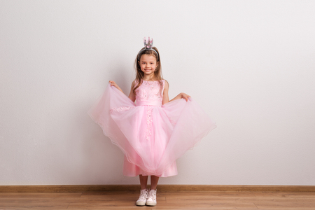 Happy small princess girl with crown headband in studio on a white background.の写真素材