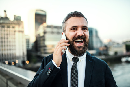 Laughing hipster businessman with smartphone in the city, making a phone call.の写真素材