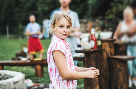 A small girl standing outdoors on a barbecue grill party in the backyard.の写真素材