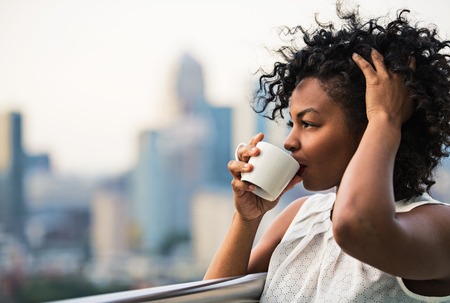 A close-up portrait of a woman standing on a terrace, drinking coffee.の写真素材