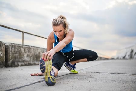 Young sporty woman runner with earphones stretching outside.