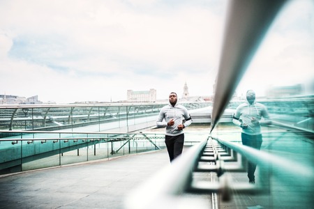 Young sporty black man runner running on the bridge outside in a city.