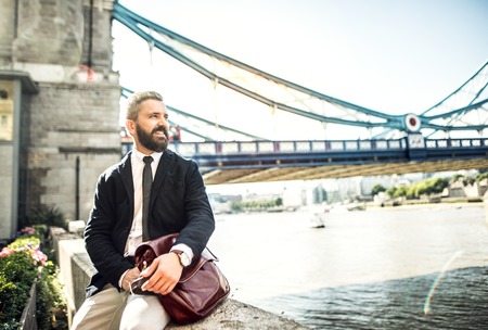 Hipster businessman with a bag sitting by the Tower Bridge in London.の写真素材