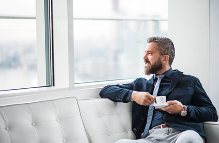 A portrait of businessman with a cup of coffee sitting on a sofa.の写真素材