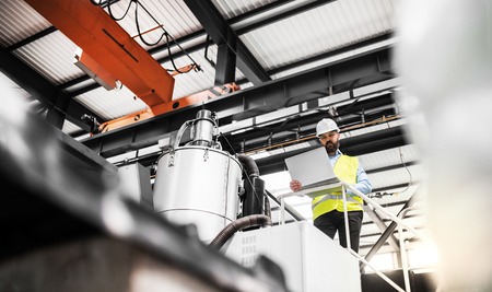 A low angle view of an industrial man engineer with laptop in a factory, working.