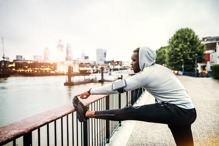 Black man runner with smartphone in an armband on the bridge in a city, stretching.の写真素材