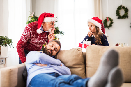 A small girl with grandfather dont want to wake up her sleeping father at Christmas time.の写真素材