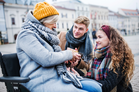Two teenagers giving a present to a grandmother in wheelchair outdoors in winter.の写真素材