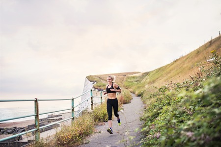 Young sporty woman runner with earphones running by sea in nature.