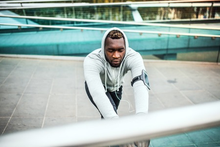 Black man runner with smartphone in an armband on the bridge in a city, stretching.の写真素材