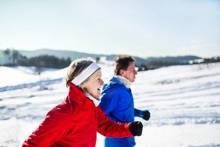 A side view of senior couple jogging in snowy winter nature.の写真素材