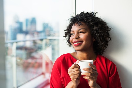 A close-up of a woman standing by the window holding coffee cup.の写真素材
