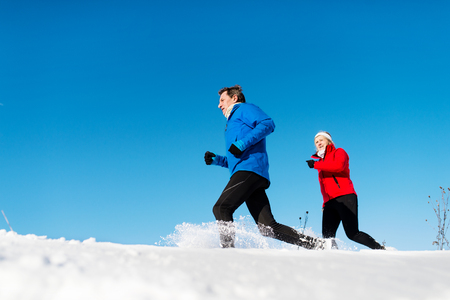 A side view of senior couple jogging in snowy winter nature.の写真素材