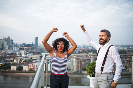 Two businesspeople standing against London view panorama, expressing excitement.の写真素材