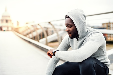 Young sporty black man runner with smart watch on the bridge in a city, resting.の写真素材