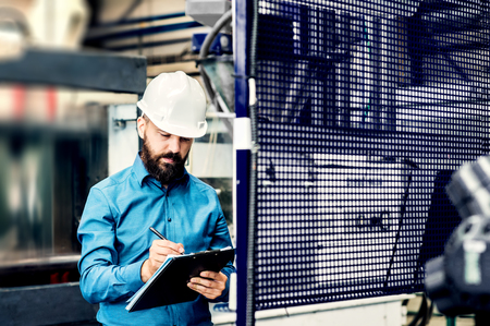 A portrait of an industrial man engineer with clipboard in a factory, working.