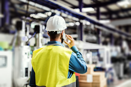 A rear view of an industrial man engineer with smartphone in a factory, working.の写真素材