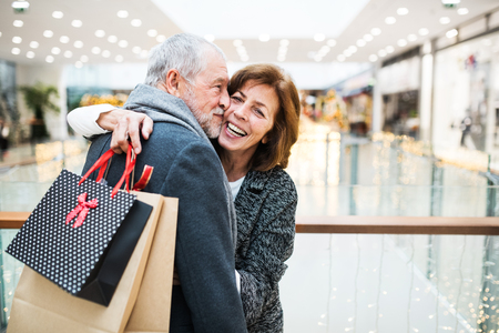Happy senior couple with paper bags in shopping center, hugging.の写真素材