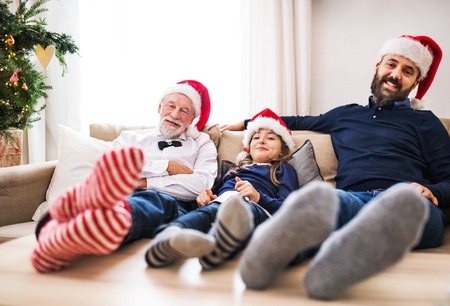 A small girl with father and grandfather sitting on a sofa at Christmas time.の写真素材