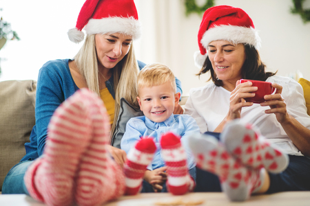 A small boy with mother and grandmother with Santa hat at home at Christmas time.の写真素材
