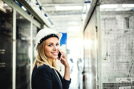 A portrait of an industrial woman engineer on the phone, standing in a factory.の写真素材