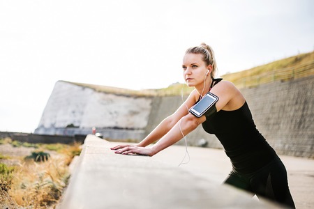 Young sporty woman runner with smartphone standing on the beach outside.の写真素材