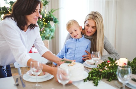 A small boy with mother looking at grandmother putting a cake on table at Christmas time.