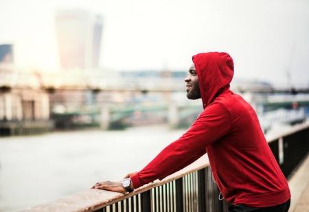 Young sporty black man runner on the bridge outside in a city, resting.