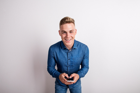 Portrait of a happy young man in a studio, holding smartphone.の写真素材