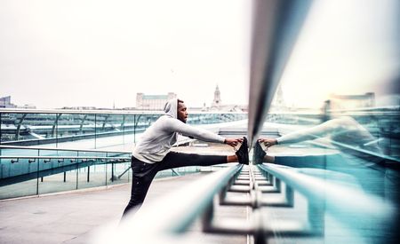 Black man runner on the bridge in a city, stretching.の写真素材